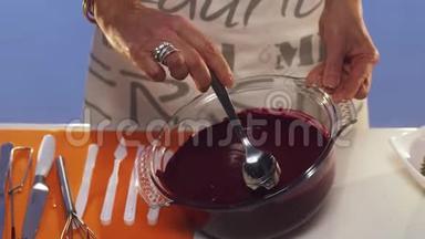 女人`她的手用勺子在桌子上的大<strong>玻璃</strong>锅里搅拌紫罗兰的物质
